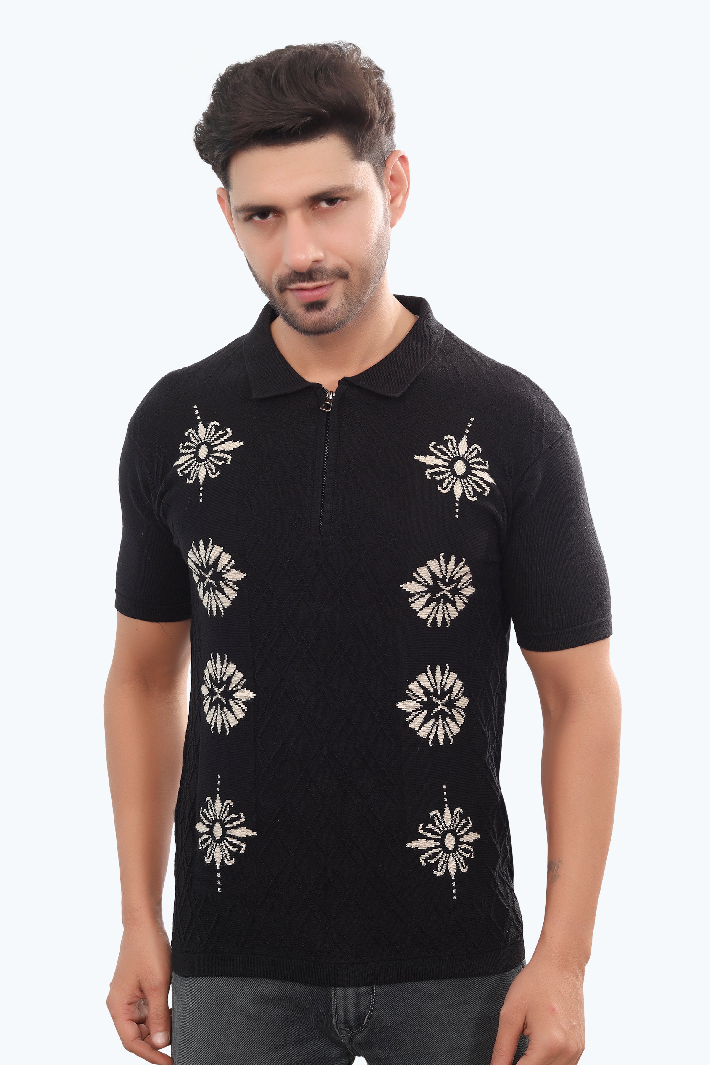 Man wearing a black polo shirt with white floral patterns on a light gray background
