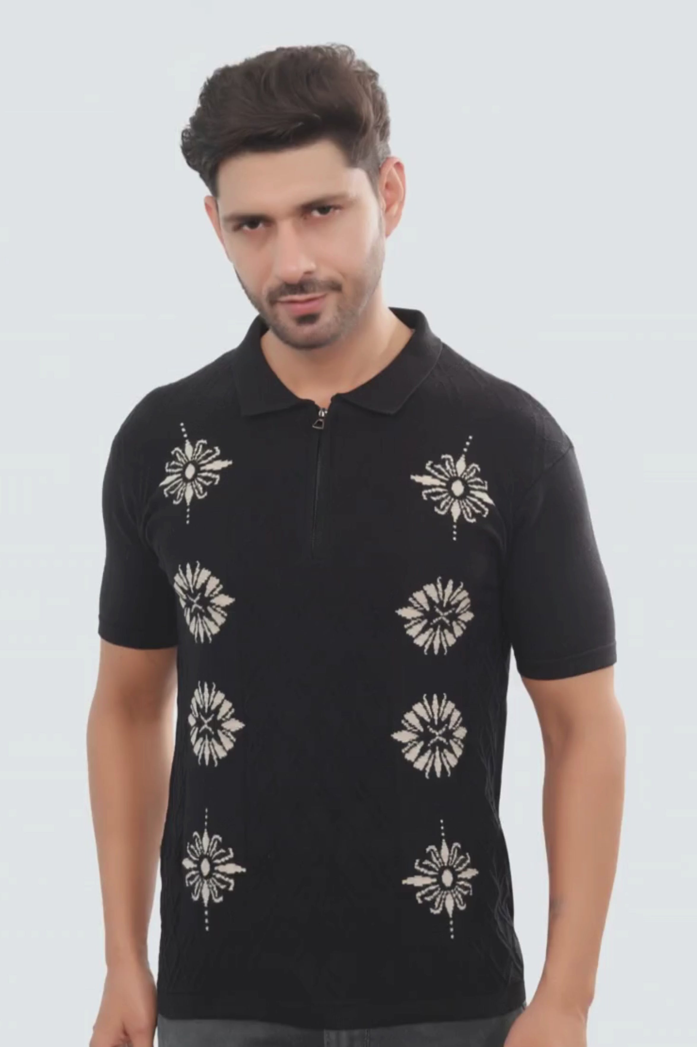 Man wearing a black polo shirt with white floral patterns on a light gray background